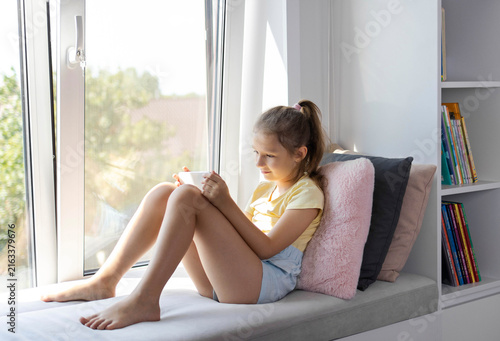 A little girl of European appearance using a tablet. The kid is playing virtual games or watching cartoons on her tablet. The child with a tablet. The problem of addiction to gadgets