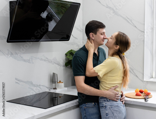 A romantic young couple sharing a tender moment, hugging and looking into each other's eyes while preparing food in their stylish home kitchen. Family home life concept.