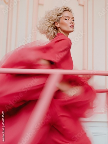 Elegant blonde woman in a flowing red dress captured in dynamic motion, creating a glamorous fashion editorial with dramatic movement, femininity and sophisticated style.