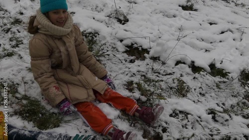 Two little girls sisters are sitting in snow in winter city park.