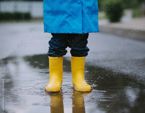 A child's feet in yellow rain boots splashing in a water puddle.