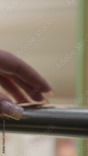 Hand with light pink speckled nails moves on metal surfaces. Nails have black speckles on light pink background. Composition centers precise actions in indoor environment