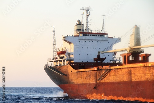 Quadro su tela Large commercial cargo ship with rusted orange hull and white superstructure sai