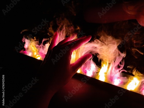 Close up of a human hand touching cool steam water vapor flames of a safe modern electric LED illuminated fireplace in the dark.