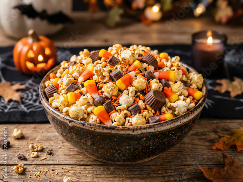 Halloween popcorn mix with candy corn, chocolate cups, and sprinkles served in rustic ceramic bowl. American carnival for Halloween celebrating concept with copy-space.