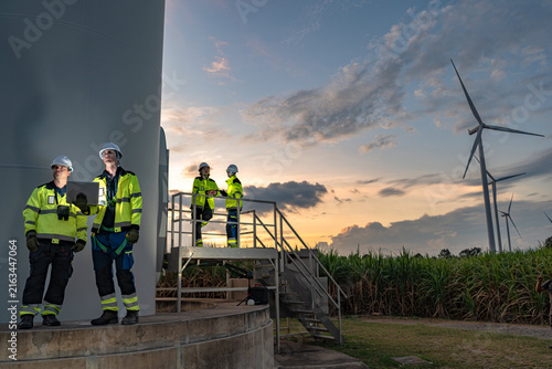 Fotografía A wind power maintenance crew wrap up a site walkover at the tower base at the base of a wind turbine among sugarcane fields in fading dusk at a renewable energy site in Thailand