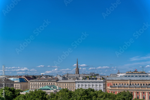 Vienna cityscape with St Stephens Cathedral spire rising above historic rooftops under blue sky