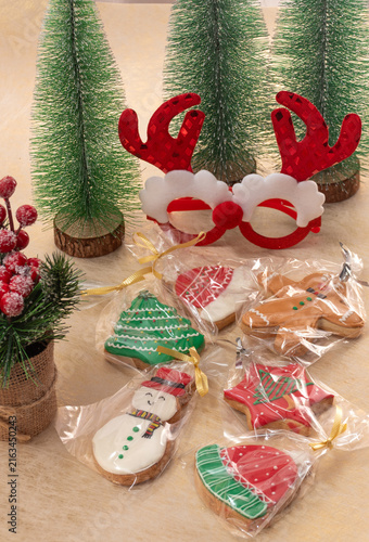 Homemade christmas cookies in various shapes, including snowman, tree, and gingerbread man, individually wrapped with ribbons, surrounded by festive holiday decorations