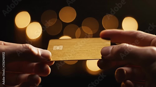 Hands holding white credit card against bokeh lights.