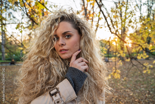 Gorgeous blonde hair girl with amazing volumized curly healthy hair, autumn portrait at sunset in the park 