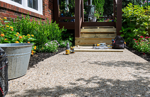 Exposed aggregate walkway leads to wooden deck steps under construction