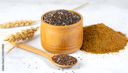 Close-up studio shot featuring chia seeds inside a wooden container, alongside a pile of spice and wheat stalks