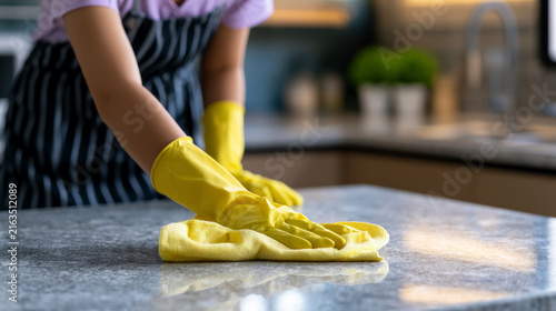 Individual wiping down kitchen countertop with a bright yellow cloth and wearing gloves in a contemporary home environment