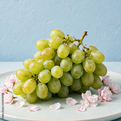 Bunch of fresh green grapes with pink flowers on plate