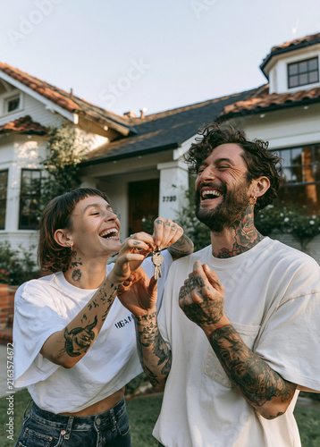 Authentic tattooed couple holding house keys in front of their new home