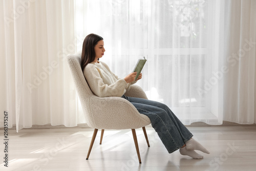 Relaxation and self care, young woman reading a book in a comfortable armchai...