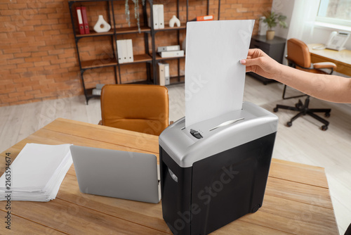 Female hand destroying paper sheet in shredder on desk in office