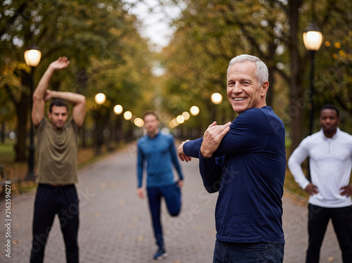 Group of diverse men stretching in an autumn park, enjoying a healthy outdoor workout together, looking at camera.