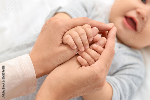 Mother holding her happy little babys hand lying on bed in bedroom, top view