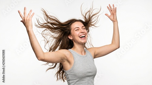 Excited young woman with long curly hair laughing with arms raised on white background