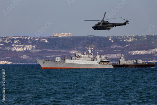 Obraz na płótnie A helicopter flies over a warship during a naval exercise in black sea near territorial waters