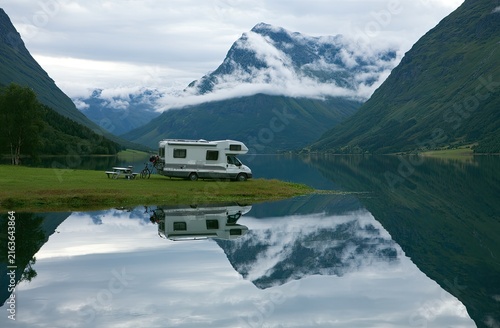 Campervan parked by tranquil lake, reflecting majestic, cloud-kissed mountains
