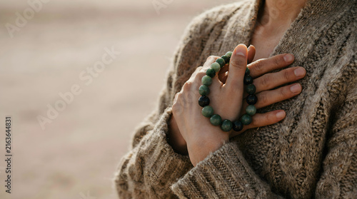 Close-up of hands displaying a natural green gemstone bead bracelet against an outdoor backdrop