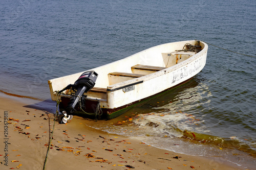 фотографія A small white motorized skiff rests along the sandy shoreline with gentle sea fo