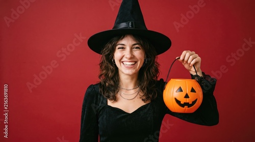 Smiling woman in witch costume holding a jack o lantern on red background