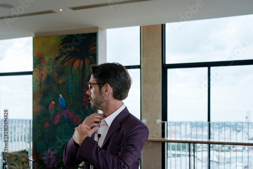 Foto A white man with glasses adjusting his clothes in a well-lit room with windows i
