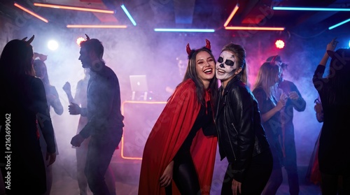Two women in halloween costumes pose at a vibrant and smoky nightclub event
