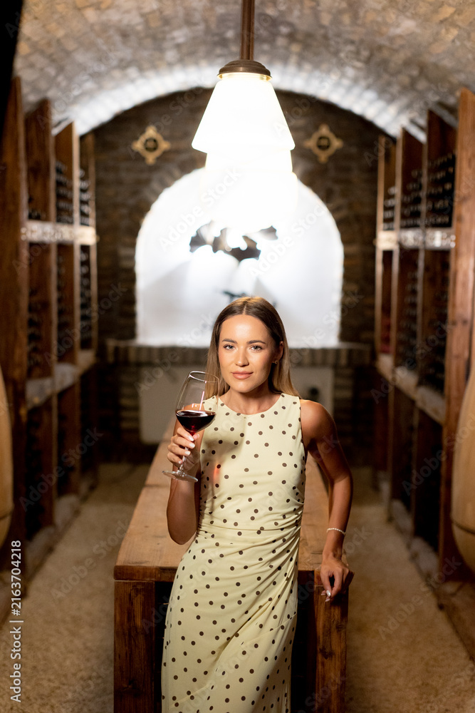 Naklejka premium Elegant woman enjoys fine wine in a cozy cellar during a tranquil evening
