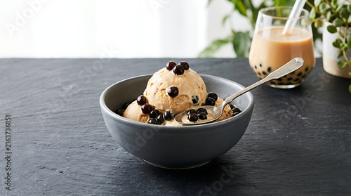 Creamy Brown Boba Ice Cream Scoops Topped with Tapioca Pearls in a Gray Bowl with a Spoon and a Boba Tea Drink in the Background