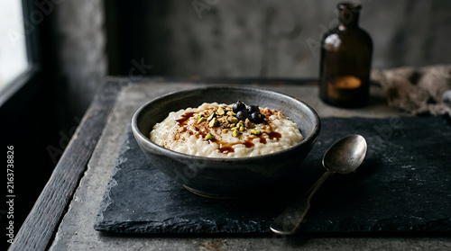 Creamy Rice Pudding Topped With Fresh Berries and Pistachios Served in a Rustic Bowl on a Textured Surface