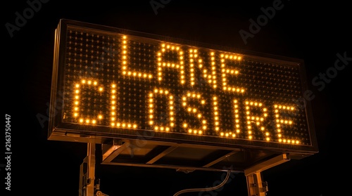 Illuminated electronic road sign displaying lane closure warning message in amber LED lights.