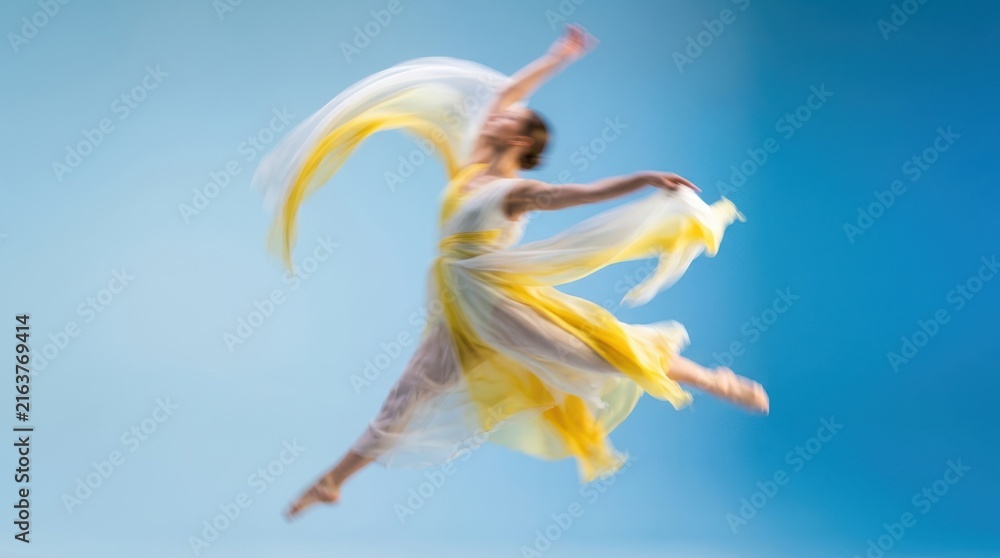Obraz premium Graceful young ballerina in a flowing yellow dress jumping and dancing through the air against a bright blue background