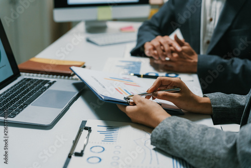 Business professionals reviewing charts and graphs on documents, discussing market strategy and financial reports in an office setting