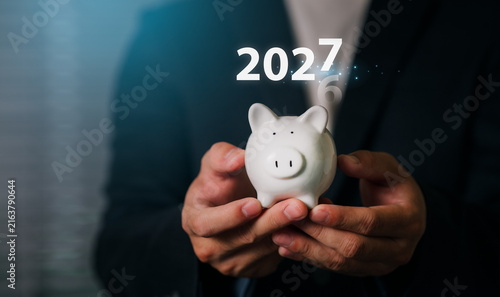 A professional businessman holding a piggy bank with a digital overlay of the year 2027, symbolizing financial growth, investment planning, and future wealth management.