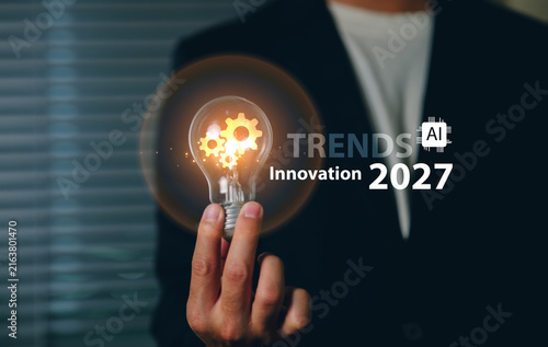 A business professional in formal attire touches a transparent light bulb innovation Trends in 2027 with gears inside, symbolizing innovation, technology, and forward-thinking in a corporate setting.