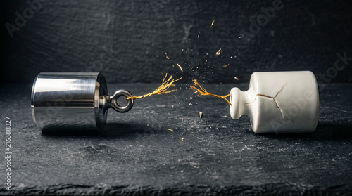 Breaking Point: A close-up shot captures the moment of fracture as a fragile porcelain object cracks under the immense pressure of a heavy metal weight, symbolizing the brink of collapse and stress.