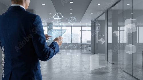 Businessman using futuristic tablet with augmented reality cloud computing icons and data network connections in modern glass corridor, digital transformation, IT infrastructure