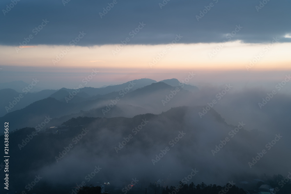 Fototapeta premium Breathtaking night and sunrise view of rolling fog, distant mountain peaks, and tea plantations in Shizhuo, Alishan, Taiwan.