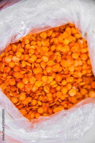 A close-up food shot showing vibrant, raw red lentils packed tightly inside a clear plastic bag, clean white background. selective focus, taken in a studio with artificial direct light at Cairo Egypt
