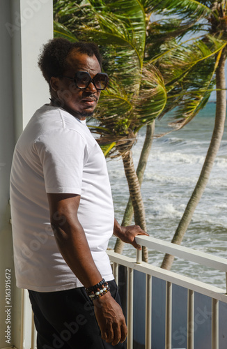 Fotografie African Man Wearing Sunglasses Standing on a Beach Balcony Looking at the Camera