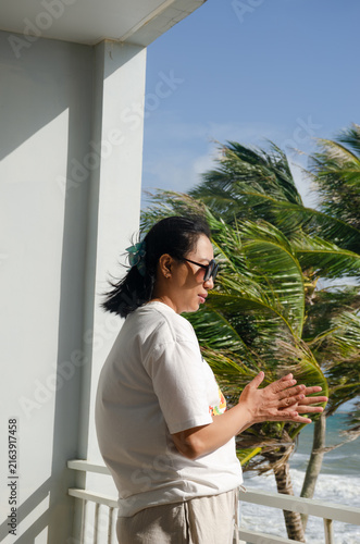 Obraz na plátně Woman Wearing Sunglasses Enjoying a Breezy Tropical Beach View From a Balcony