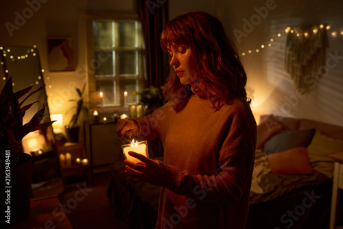 Caucasian young adult woman lighting candle in bedroom  practicing self care and mindfulness. Image represents mental wellbeing and relaxation  suitable for lifestyle marketing