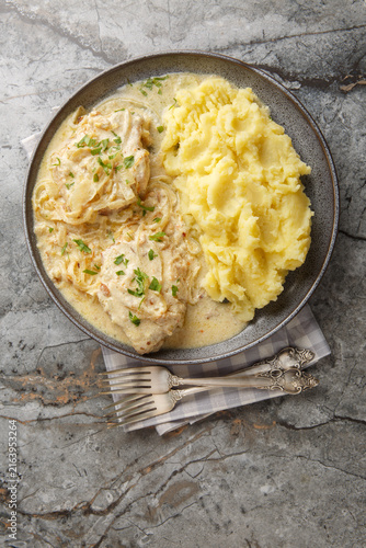 German schnitzel with onion cream sauce and mashed potatoes garnish close-up in a plate on the table. Vertical top view from above