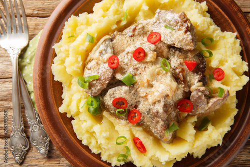 Homemade fried liver with onions and sour cream served with mashed potatoes close-up in a plate on the table. Horizontal top view from above
