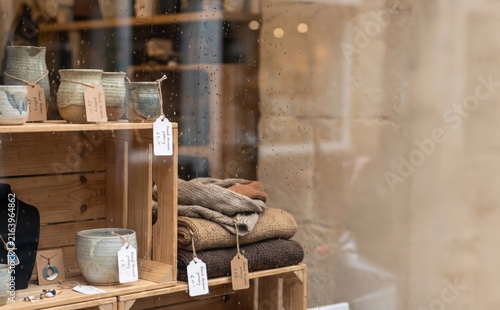 Handmade pottery and knitted garments displayed in a cozy boutique shop window on a rainy day