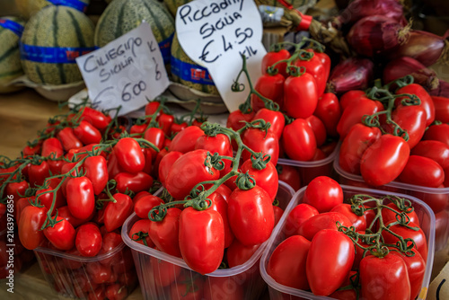 Fresh local cuor di bue oxheart tomatoes in a woven basket with a handwritten price sign on display at a farmers market stall in Sanremo, Italy
